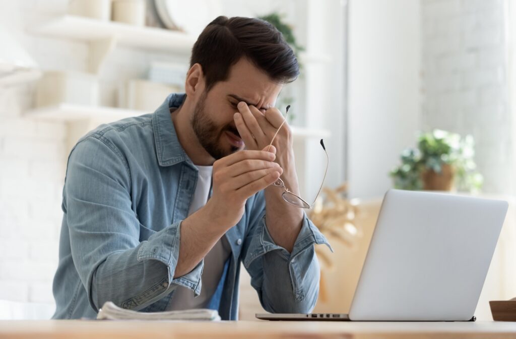 a man is rubbing his eyes in front of a computer due to digital eye strain.