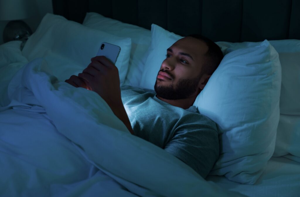 A young man laying in his bed is focused on his smartphone before sleeping.