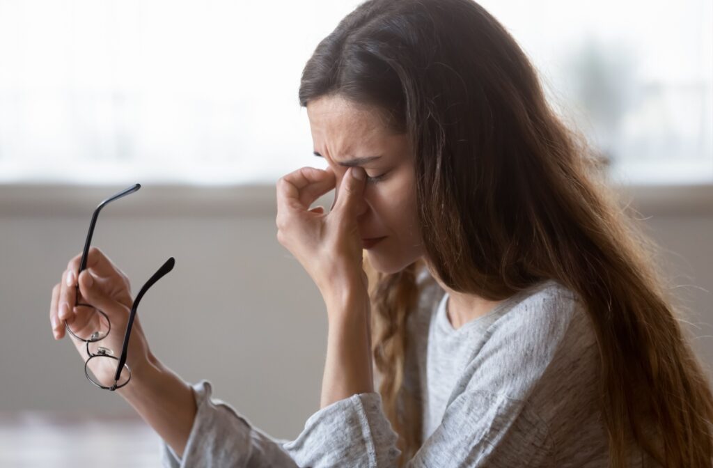 A young woman taking off her glasses to rub her eyes due to discomfort from meibomian gland dysfunction.