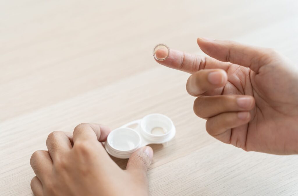 A close-up of a person's hand holding up a contact lens on the tip of their finger.