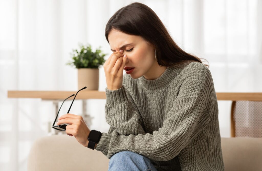 A woman taking off her glasses and rubbing her eyes in frustration due to dry eye discomfort.